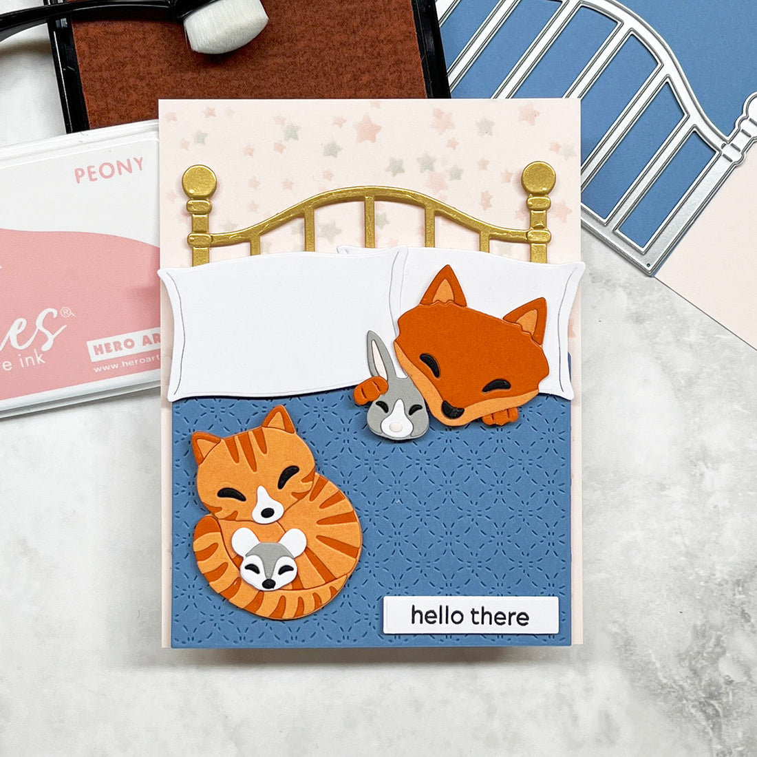 Handmade card featuring a die cut fox and orange tabby cat in  a brass bed  with a blue quilt.